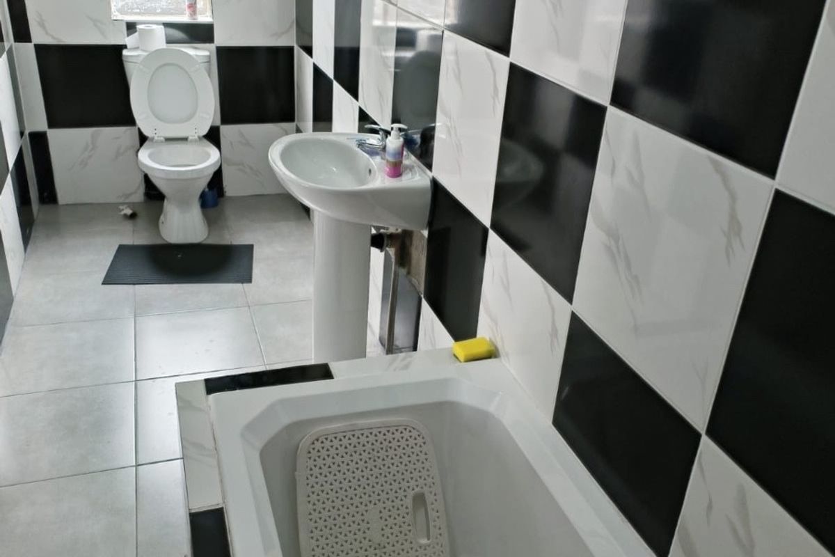 A bathroom featuring a bathtub, pedestal basin, and toilet, finished with high-contrast black and white checkered wall tiling.
