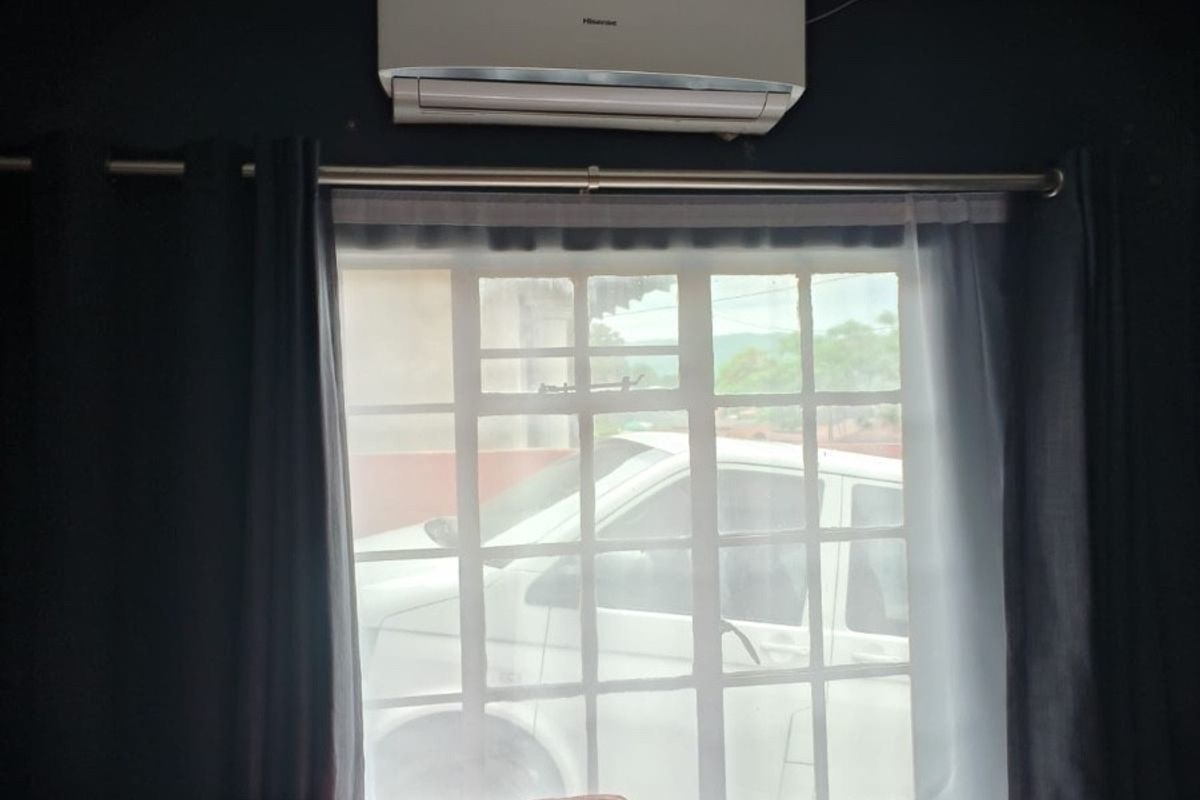 A living room interior featuring a wall-mounted split-system air conditioning unit and a grid-pattern window with curtains.