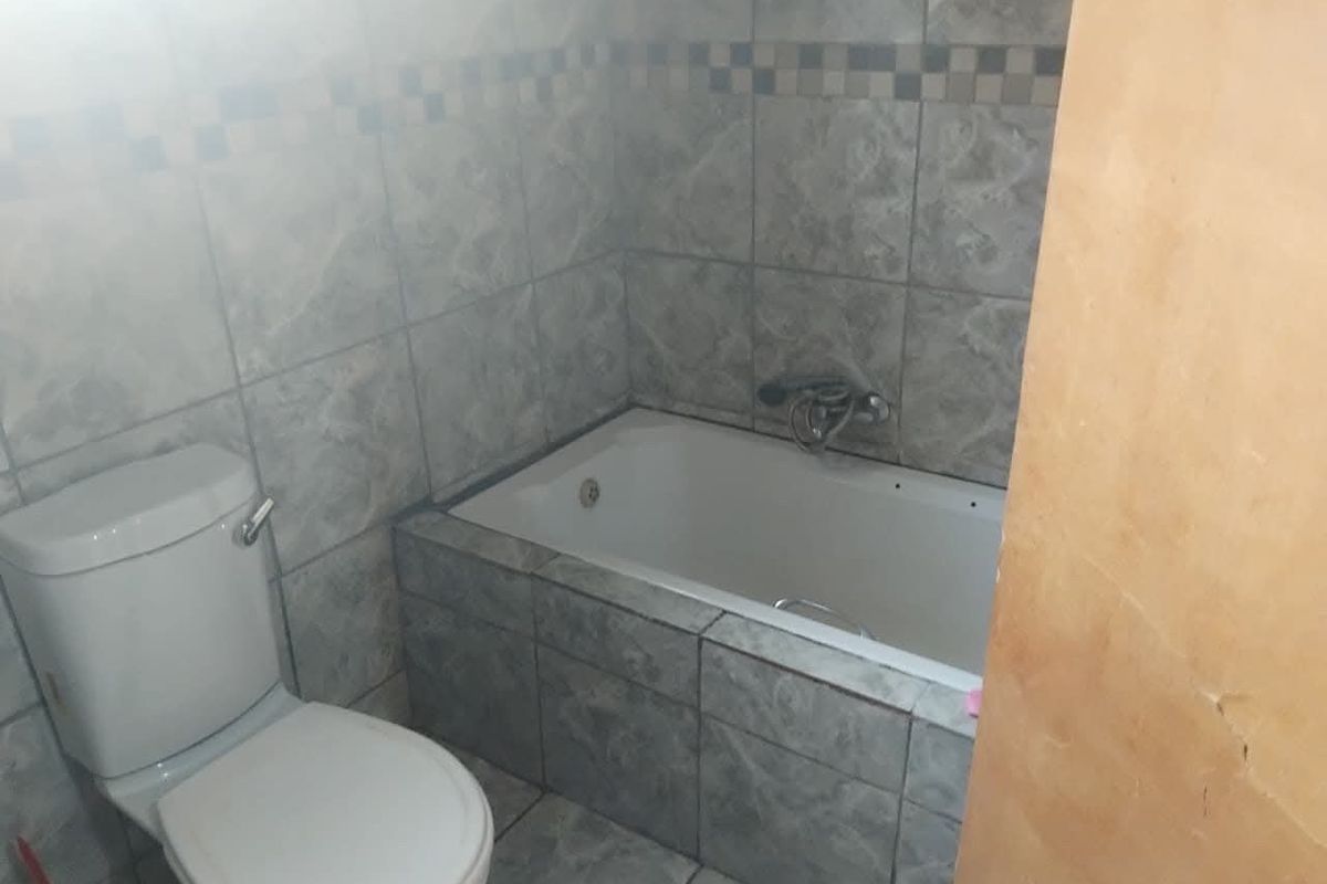 A functional bathroom featuring a built-in bathtub and toilet with full-height wall tiling and tiled flooring.