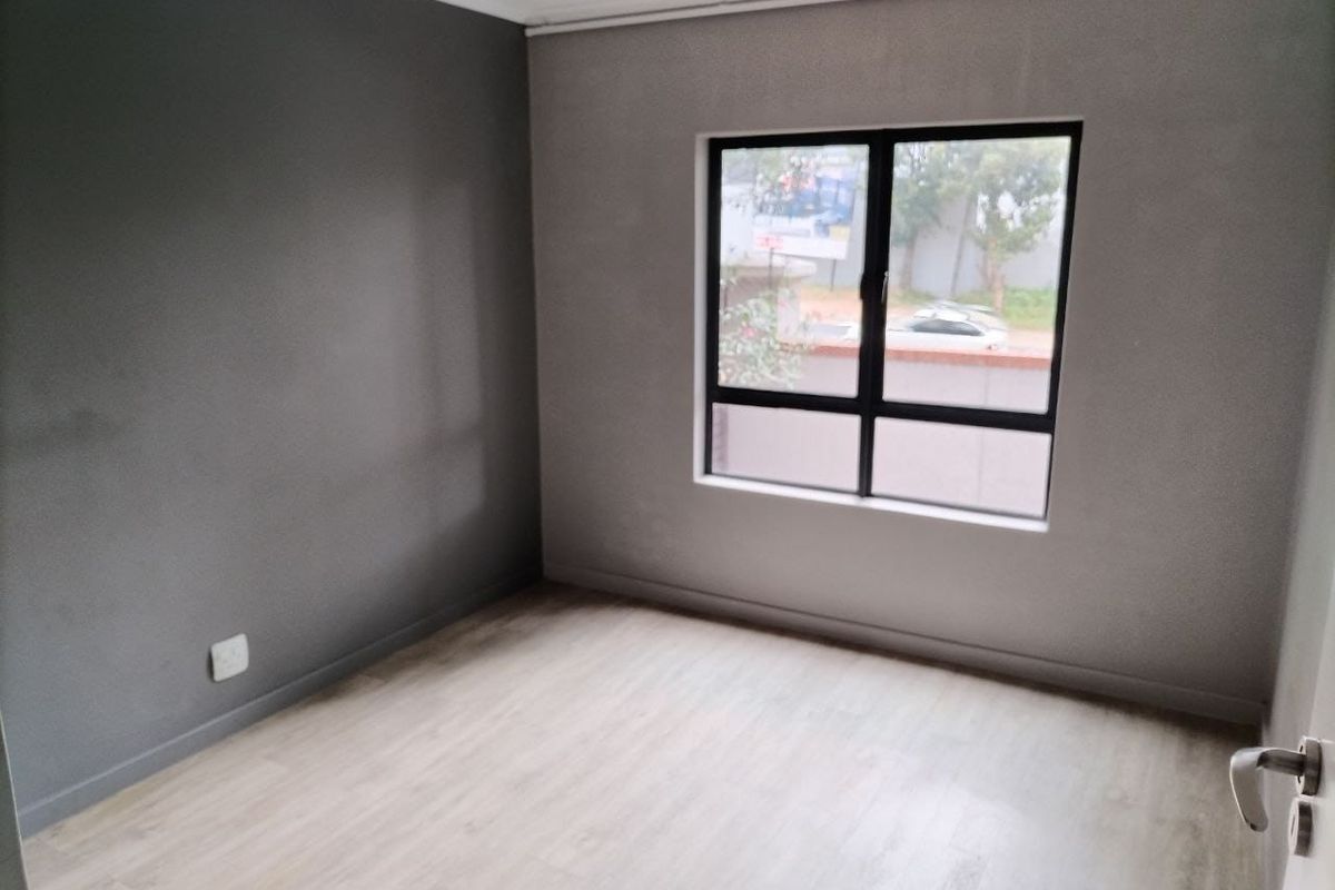 A clean, empty bedroom featuring modern grey painted walls, light-toned laminate flooring, and a large aluminium-framed window.