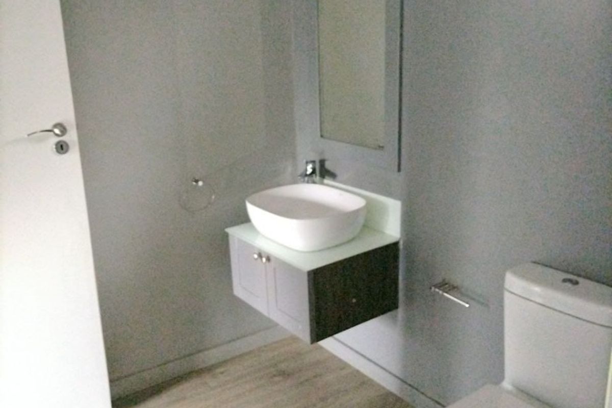 A modern, minimalist bathroom featuring a wall-mounted vanity with a vessel sink, a toilet, and light-toned laminate flooring.