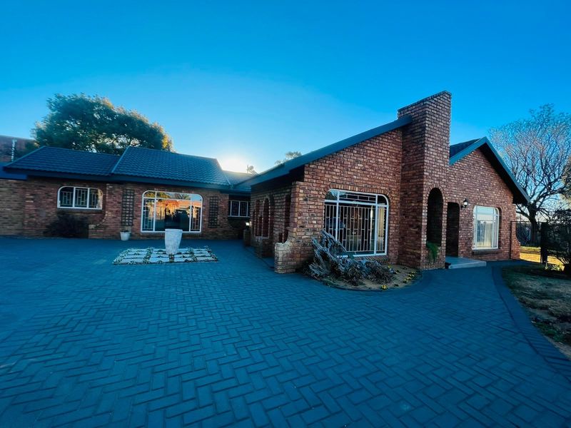 A well-maintained face-brick house featuring a large paved driveway, arched entrance, and secure window treatments under a dark tiled roof.