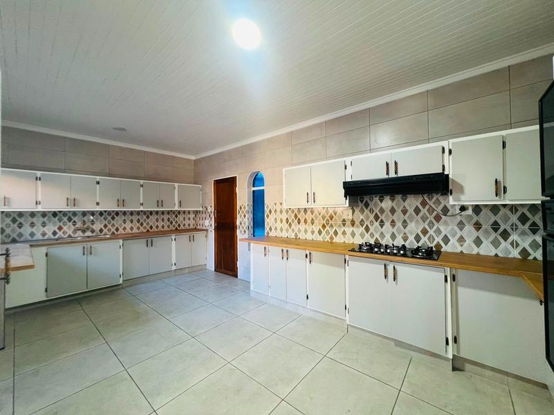 Spacious kitchen featuring extensive built-in cabinetry, laminate countertops, a gas hob with extractor fan, and decorative tiled backsplash.
