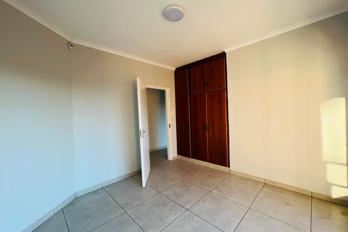 A clean, empty bedroom featuring neutral tiled flooring and dark wood built-in cupboards, offering a blank canvas for personalization.