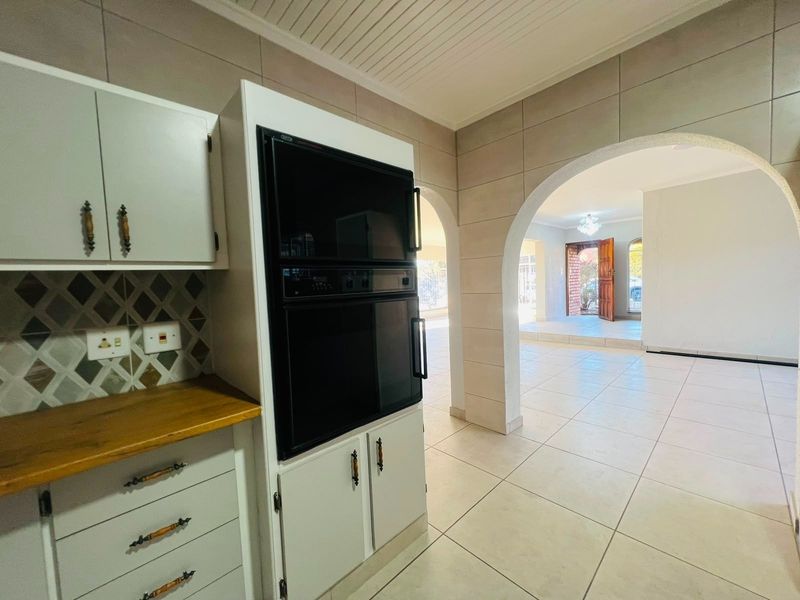 A clean, empty kitchen area featuring a built-in double oven, wooden countertops, and tiled finishes, leading through an archway into the main living space.