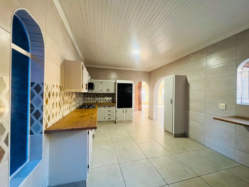 A spacious, empty kitchen featuring built-in cabinetry, a wooden countertop, gas hob, built-in oven, and tiled finishes with distinctive arched architectural details.