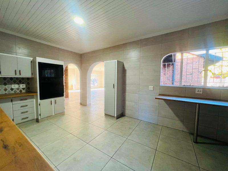 A spacious, tiled kitchen featuring built-in oven cabinetry, a breakfast bar, and distinctive archways leading to the adjacent living area.