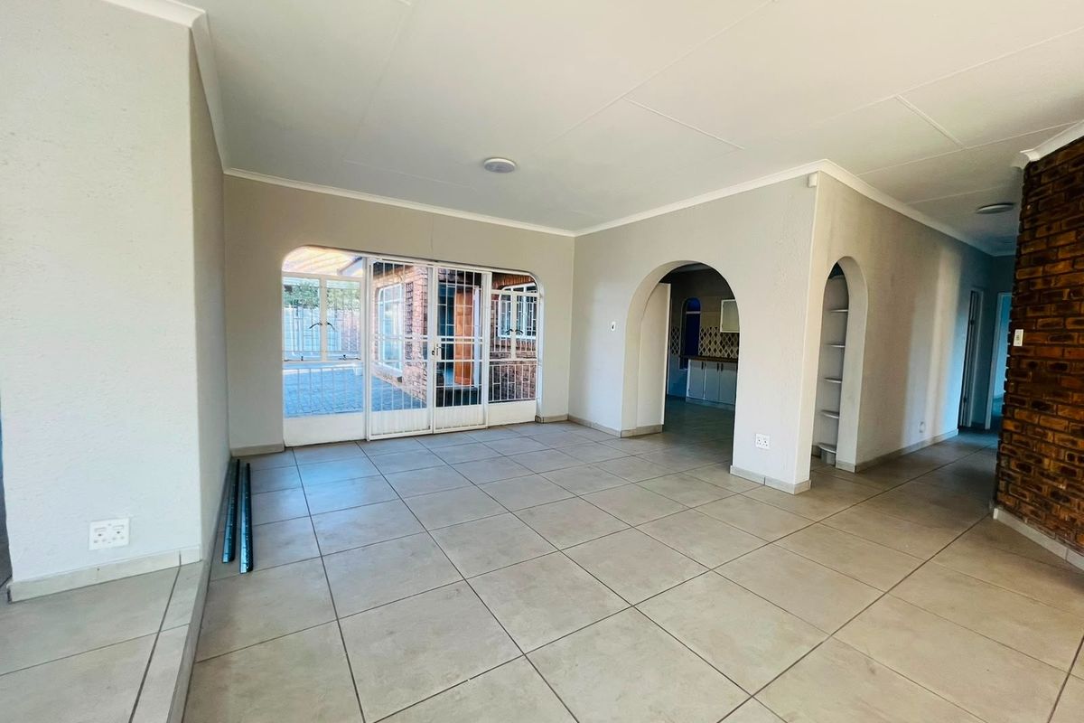 Spacious, open-plan living area featuring neutral tiled flooring, arched architectural details, and an exposed brick feature wall, leading to an outdoor patio area.