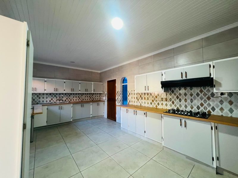 Spacious kitchen featuring extensive built-in cabinetry, wooden countertops, a gas hob with extractor fan, and neutral tiled finishes throughout.