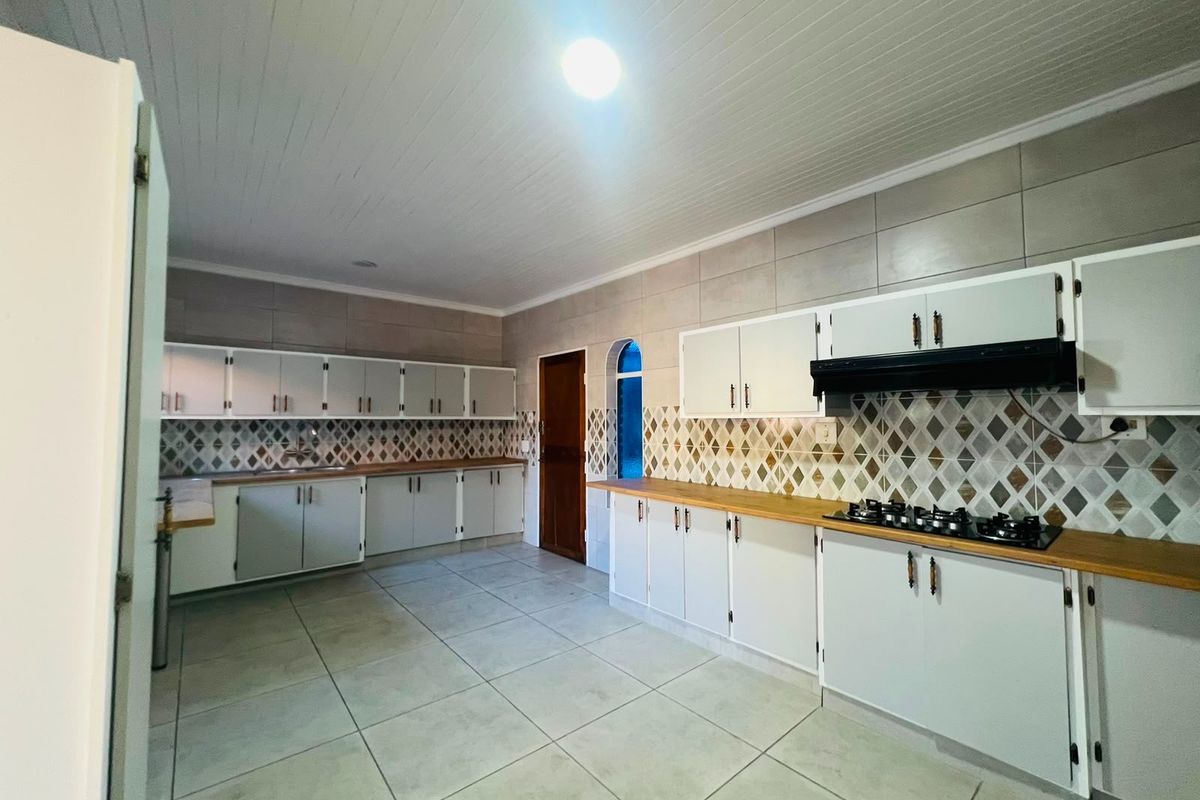 Spacious kitchen featuring extensive built-in cabinetry, wooden countertops, a gas hob with extractor fan, and neutral tiled finishes throughout.