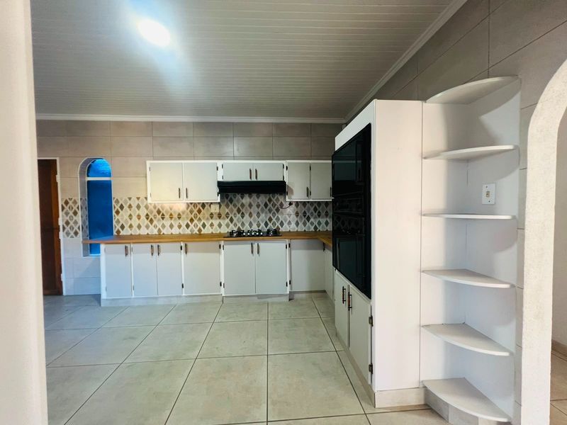 A spacious kitchen featuring white built-in cabinetry, wooden countertops, a gas hob with extractor, and tiled finishes throughout.