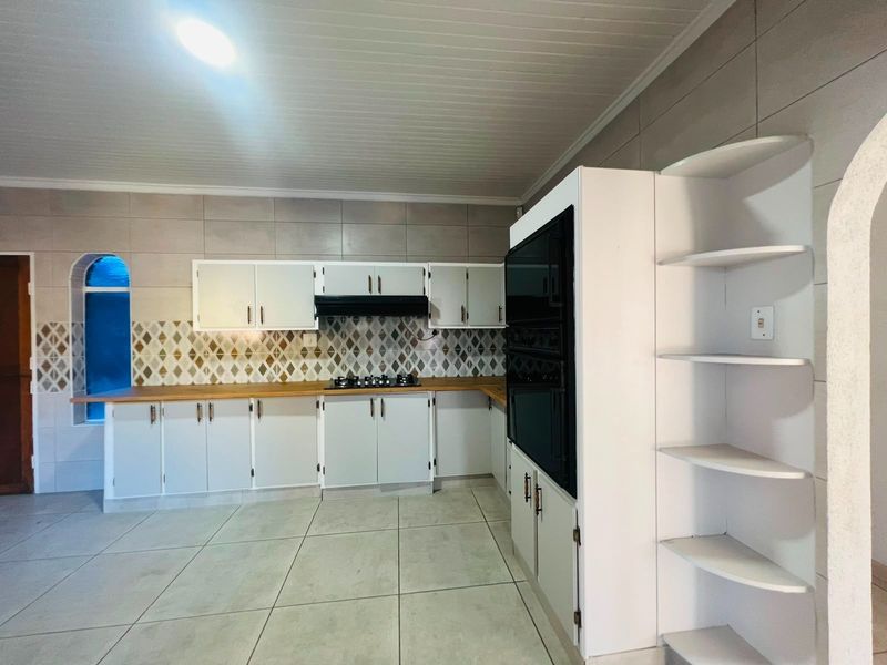 A functional kitchen featuring white cabinetry, wooden countertops, a gas hob, and a built-in oven, finished with tiled flooring and a decorative backsplash.