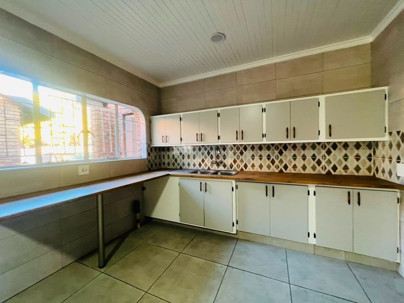 A functional kitchen featuring built-in cabinetry, a double sink, timber countertops, and a decorative tiled backsplash with ample natural light.