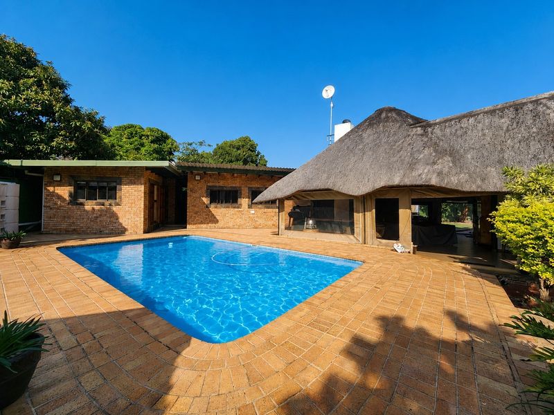 Outdoor pool area featuring a swimming pool, brick paving, and a covered patio with a traditional thatched roof.