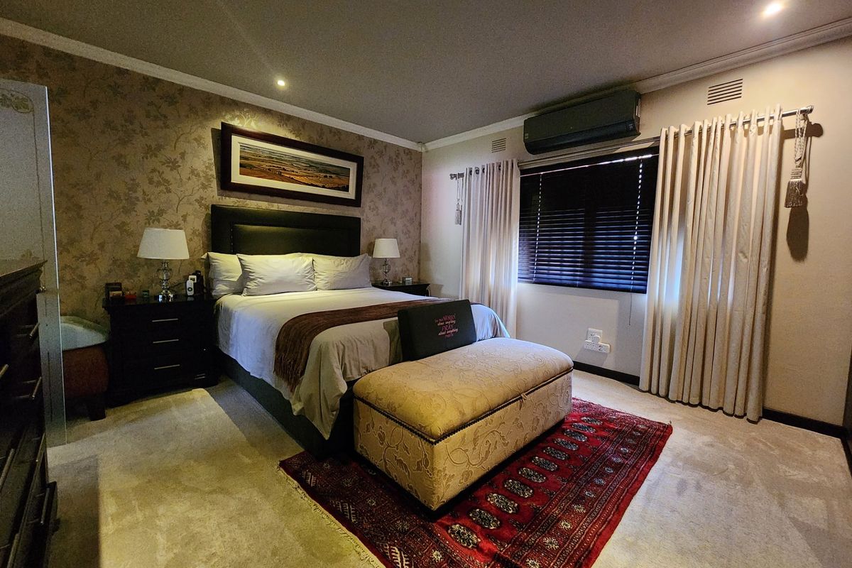 A well-maintained bedroom featuring a wallpapered accent wall, recessed lighting, carpeted flooring, and a wall-mounted air conditioning unit.