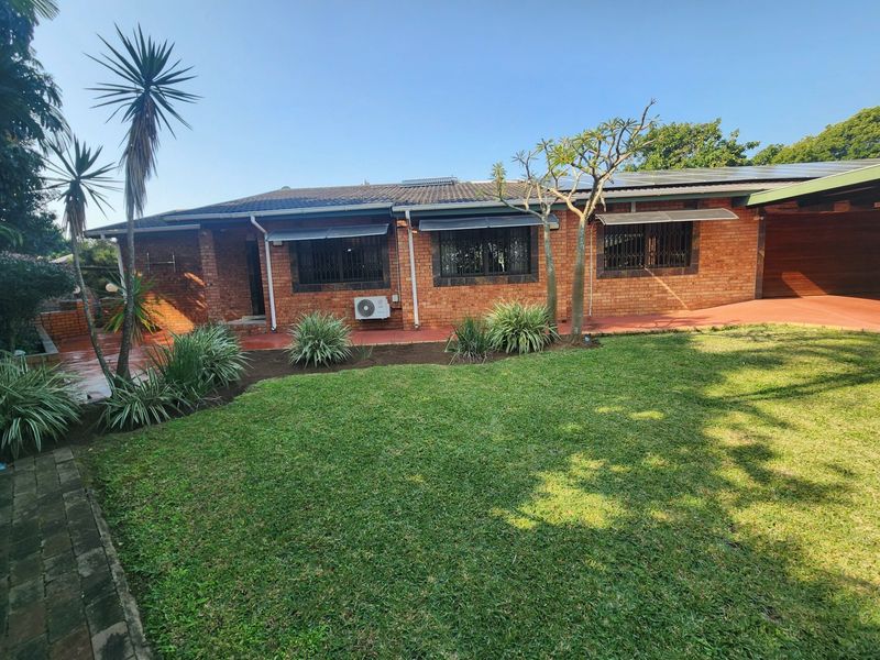 Rear view of a face brick house featuring a tiled roof with solar panels, security bars on windows, and a well-maintained lawn and patio area.