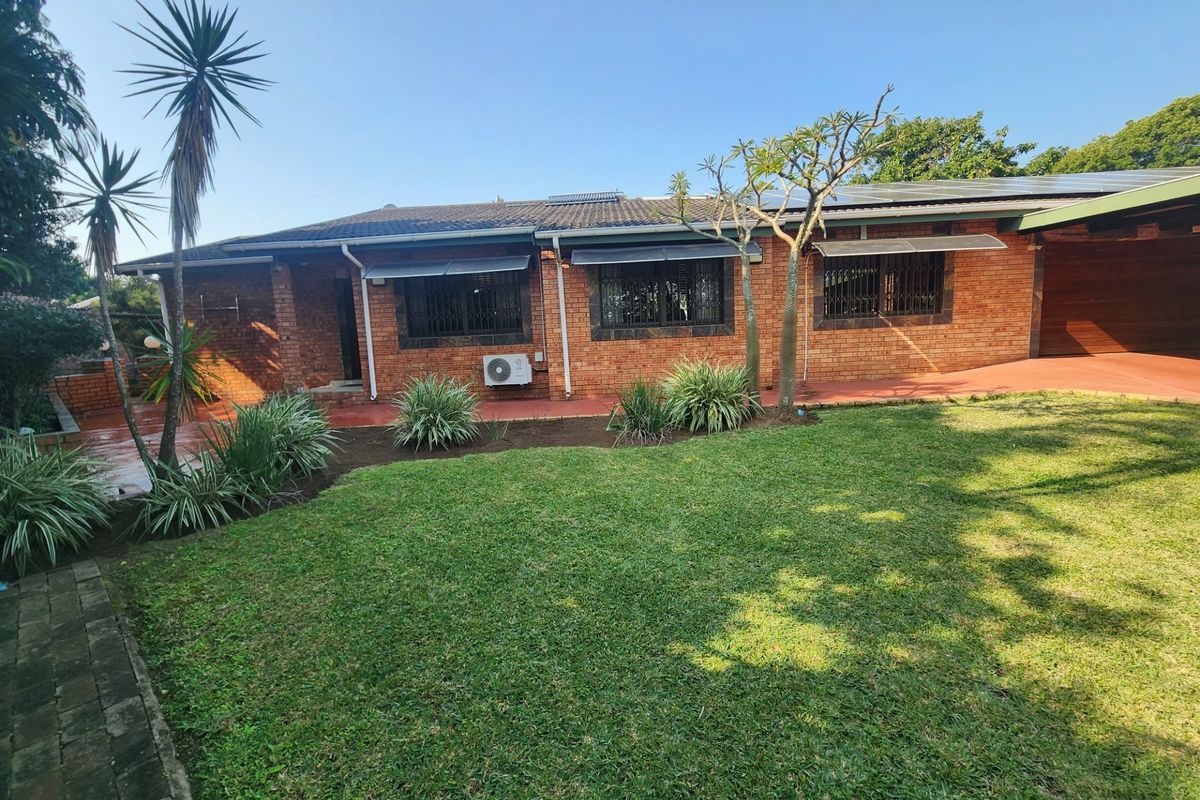 Rear view of a face brick house featuring a tiled roof with solar panels, security bars on windows, and a well-maintained lawn and patio area.