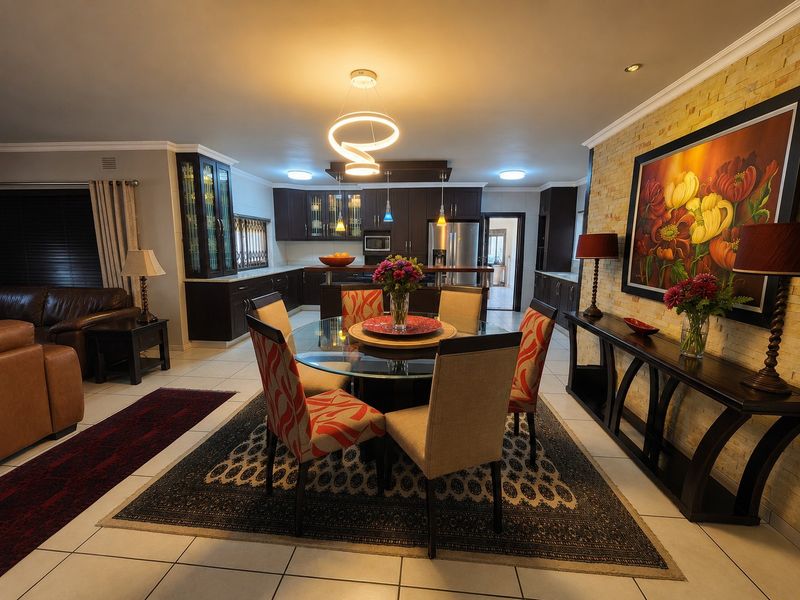Spacious open-plan living and dining area featuring a modern kitchen with dark cabinetry, a stone feature wall, and contemporary lighting fixtures.