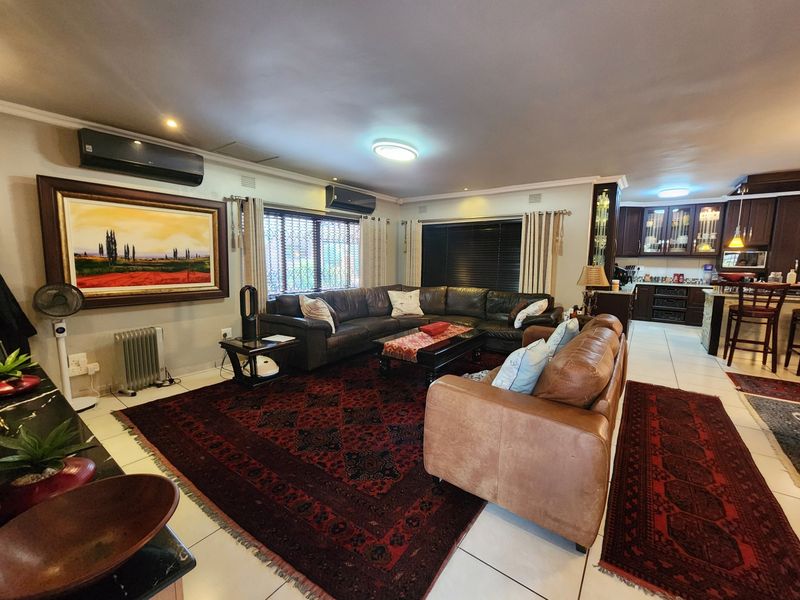 Spacious open-plan living area featuring tiled floors, integrated air conditioning, and a well-appointed kitchen with dark wood cabinetry and a central island.