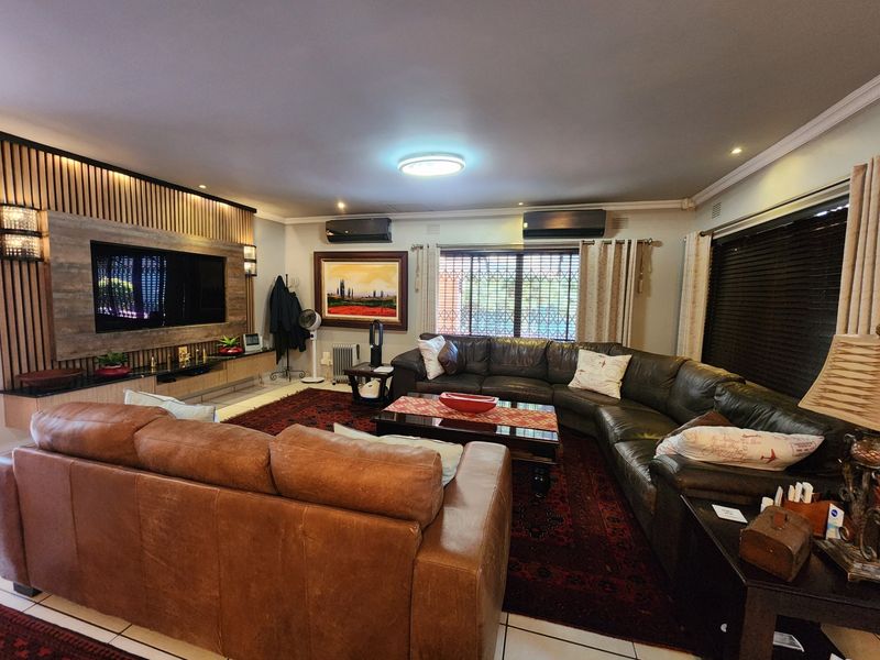 Spacious living room featuring a custom built-in media wall with timber slat detailing, dual air conditioning units, and large windows with security bars.