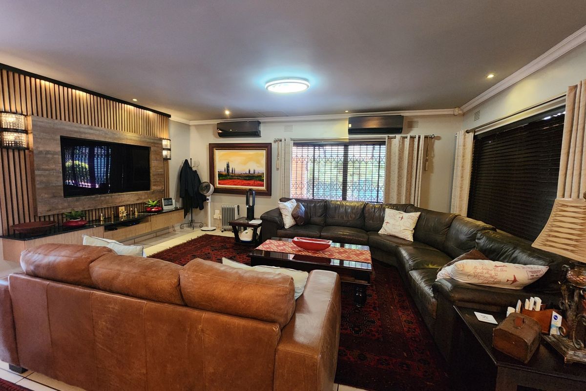 Spacious living room featuring a custom built-in media wall with timber slat detailing, dual air conditioning units, and large windows with security bars.