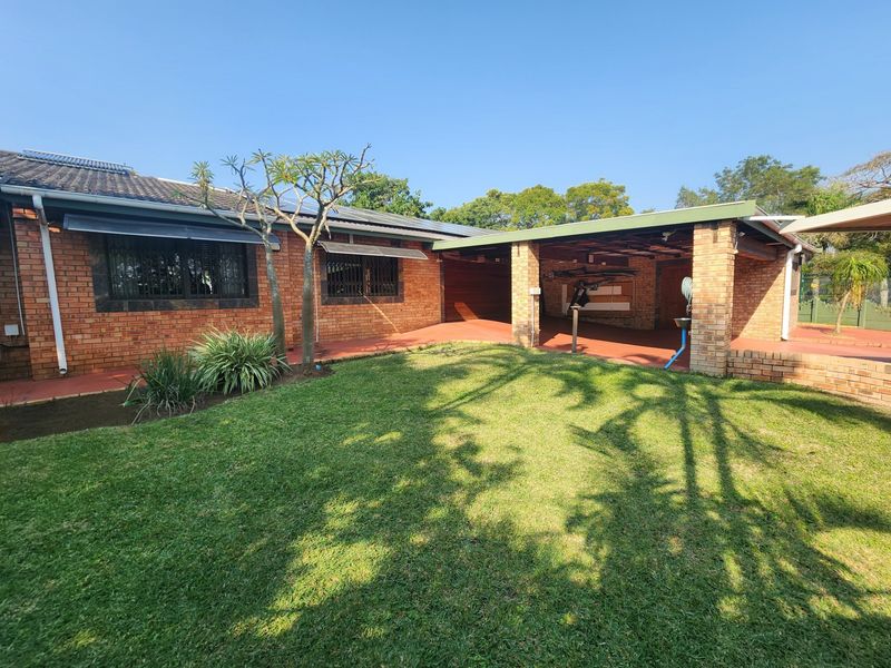 A well-maintained rear exterior view featuring a face brick facade, a covered patio area, and a neat lawn with solar water heating infrastructure.