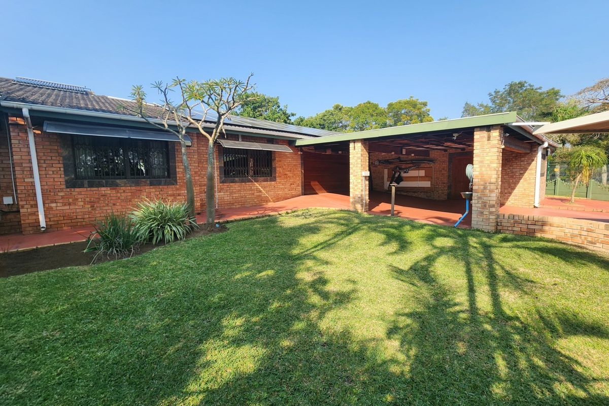 A well-maintained rear exterior view featuring a face brick facade, a covered patio area, and a neat lawn with solar water heating infrastructure.