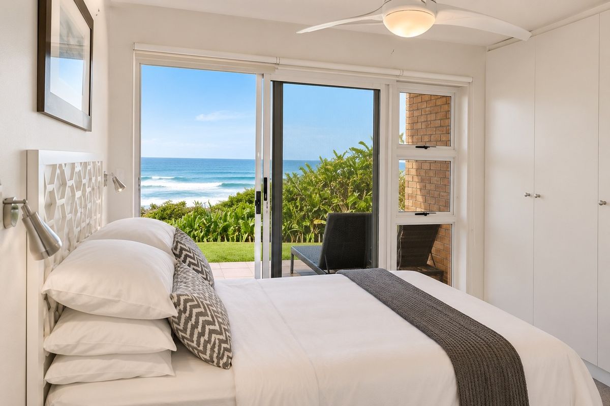 Bright bedroom featuring a built-in wardrobe, ceiling fan, and sliding glass doors that open to a patio with direct ocean views.
