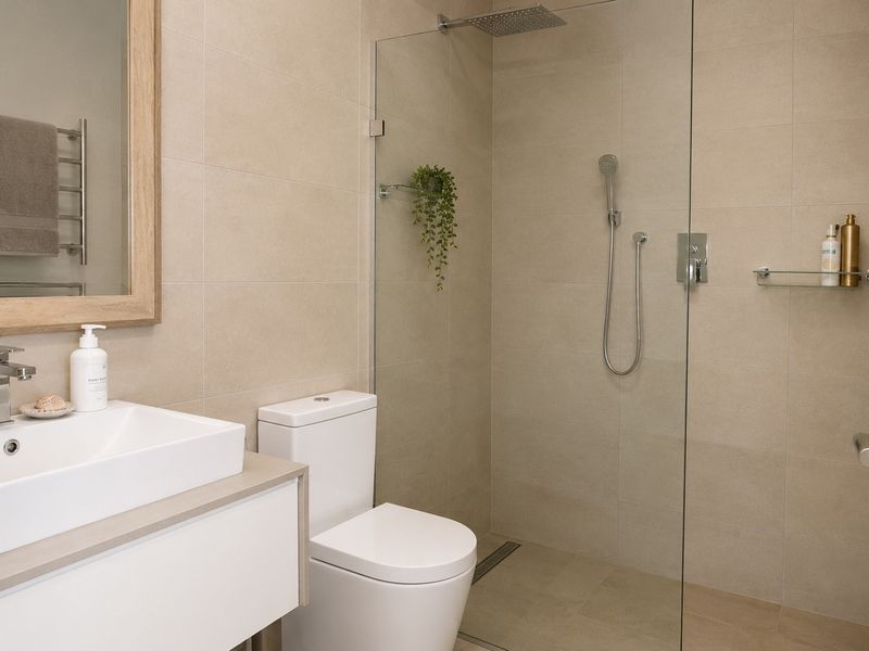 Modern bathroom featuring a walk-in shower with glass screen, wall-mounted vanity basin, toilet, and a heated towel rail with neutral tiling.
