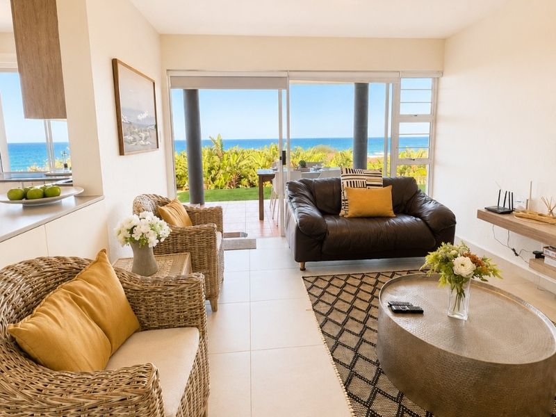 Bright open-plan living area featuring tiled floors and large sliding glass doors that open to a scenic ocean view.