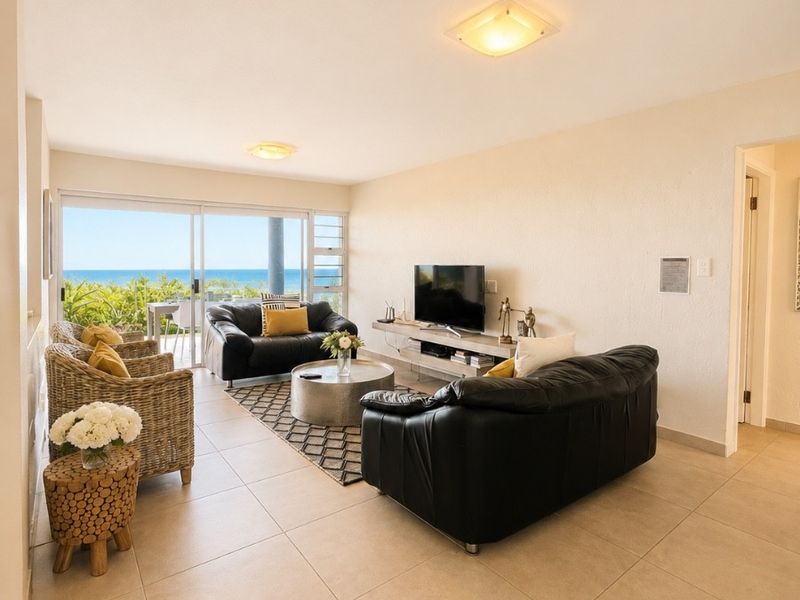 Spacious living room featuring neutral tiled flooring and large sliding glass doors that provide natural light and access to an outdoor balcony with ocean views.