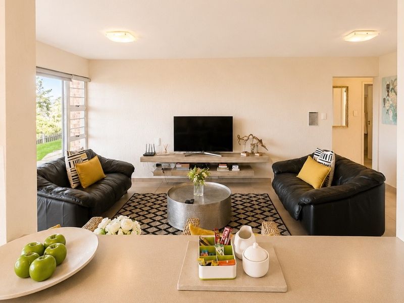 Open plan living area featuring a stone kitchen breakfast bar overlooking a comfortable lounge space with a floating media console and large windows.