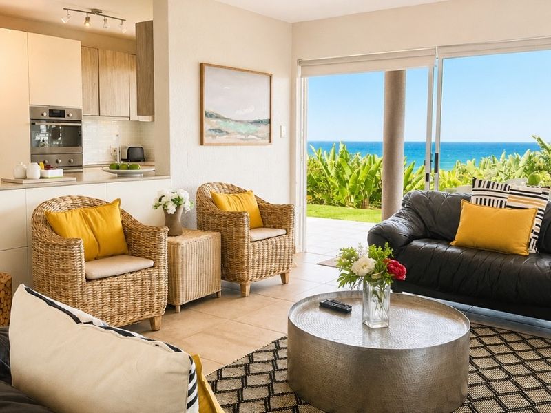 Open-plan living area featuring a modern kitchen with built-in appliances, flowing seamlessly to a patio with stunning ocean views through large sliding doors.