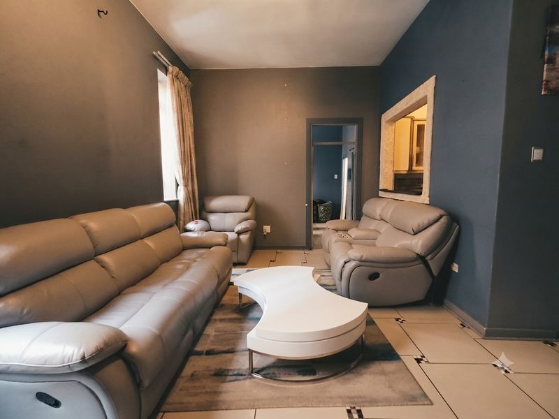 A living room featuring tiled flooring and a pass-through window connecting to the kitchen area, requiring some cosmetic maintenance.