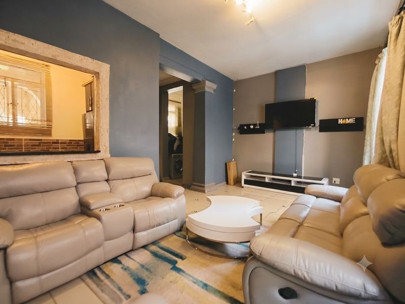 A living room featuring tiled floors, a decorative column, and a pass-through window connecting to the kitchen area.