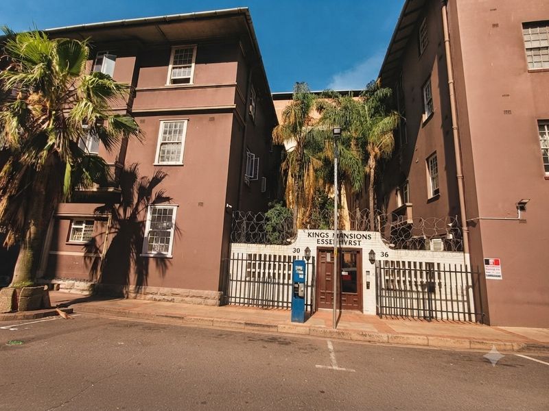 Street-level view of the Kings Mansions apartment building entrance, featuring secure gated access, perimeter fencing with razor wire, and traditional sash window detailing.