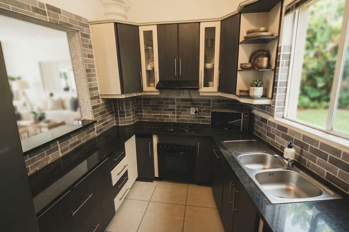 A well-maintained kitchen featuring dark cabinetry, granite countertops, a double stainless steel sink, and a tiled backsplash with a built-in oven and hob.