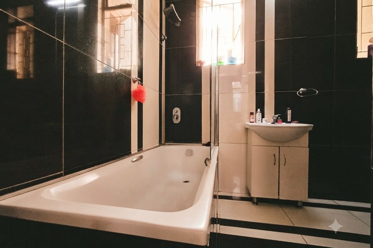 A bathroom featuring a bathtub, shower fixture, and a vanity unit with a washbasin, finished with high-contrast black and white wall and floor tiles.