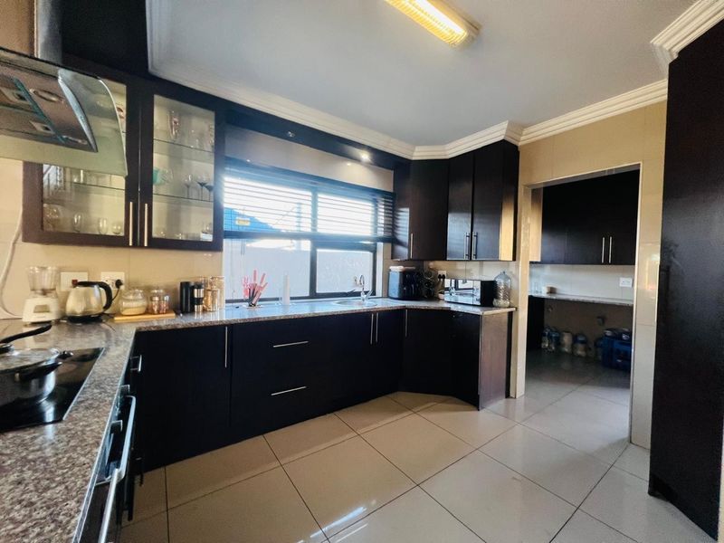A functional kitchen featuring dark wood cabinetry, granite countertops, and a separate scullery area, finished with modern ceramic floor tiles.