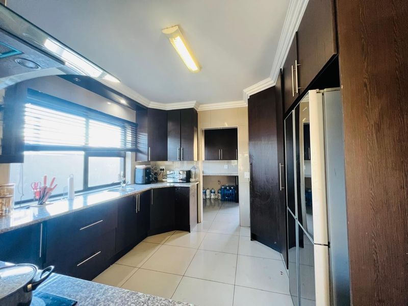 A functional kitchen featuring dark wood cabinetry, granite countertops, and a separate scullery area, complemented by tiled flooring and modern lighting.