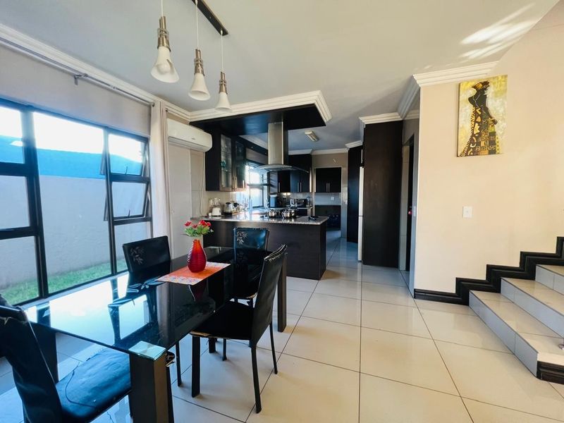 Open-plan kitchen and dining area featuring dark cabinetry, granite countertops, tiled flooring, and direct access to a staircase.