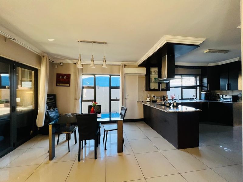Spacious open-plan living and dining area featuring a modern kitchen with dark cabinetry, granite countertops, and direct access to the outdoor patio area.