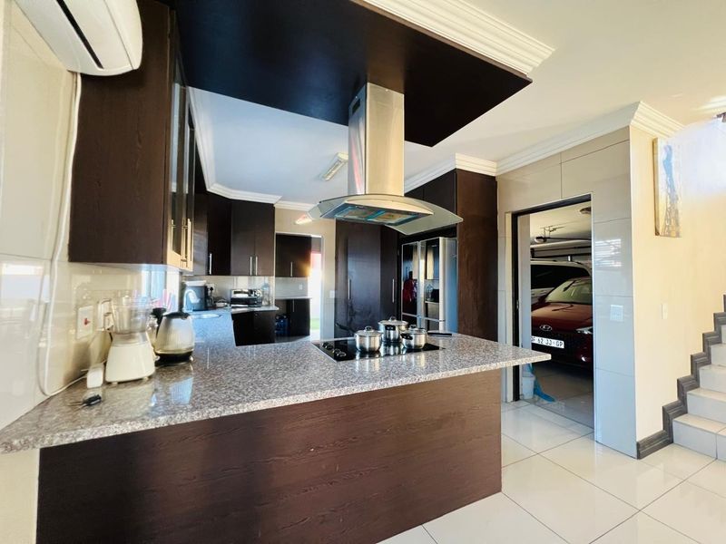Modern kitchen featuring dark wood cabinetry, granite countertops, a central island with an electric hob, and a stainless steel extractor fan.