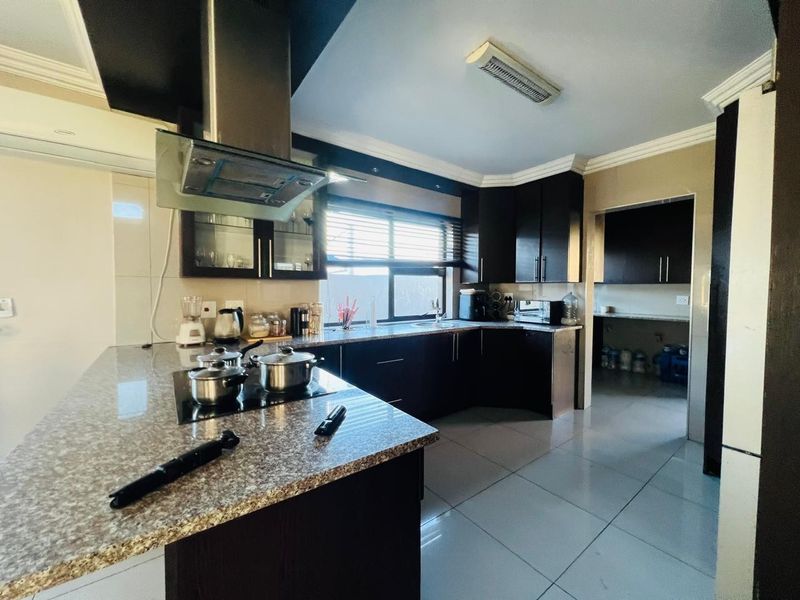 Modern kitchen featuring dark cabinetry, granite countertops, an electric hob with extractor fan, and an adjoining scullery area with tiled flooring throughout.