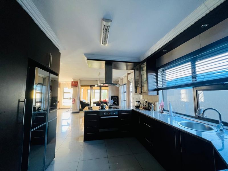 Modern kitchen featuring dark cabinetry, granite countertops, built-in oven, stainless steel extractor fan, and tiled flooring, flowing into an open-plan living area.