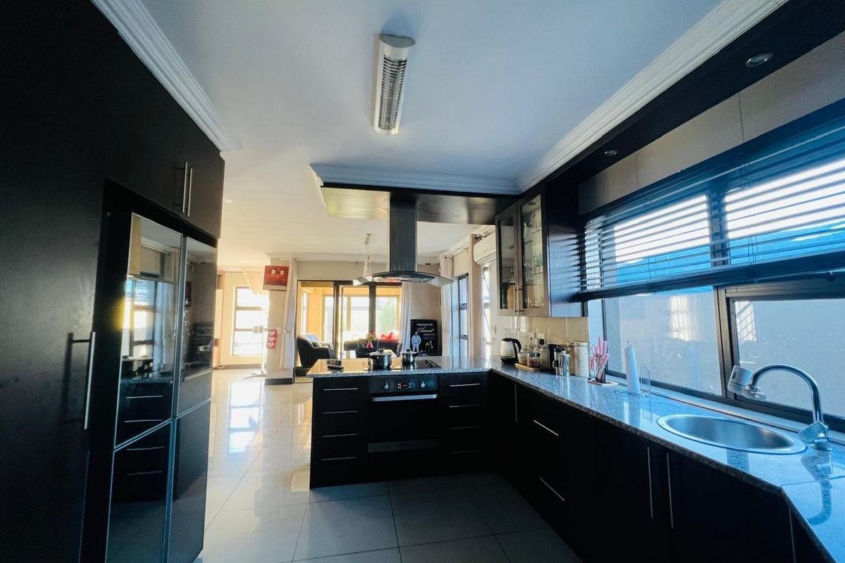 Modern kitchen featuring dark cabinetry, granite countertops, built-in oven, stainless steel extractor fan, and tiled flooring, flowing into an open-plan living area.