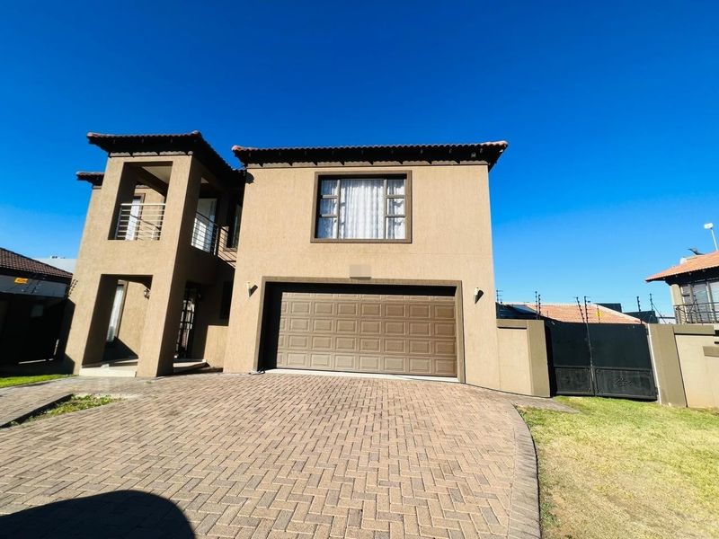 A well-maintained double-story residential property featuring a paved driveway, integrated double garage, and a balcony, secured with boundary walls and electric fencing.