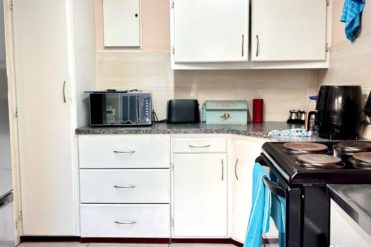A compact kitchen featuring white built-in cabinetry, laminate countertops, and tiled backsplash, requiring cosmetic updates to modernize the space.