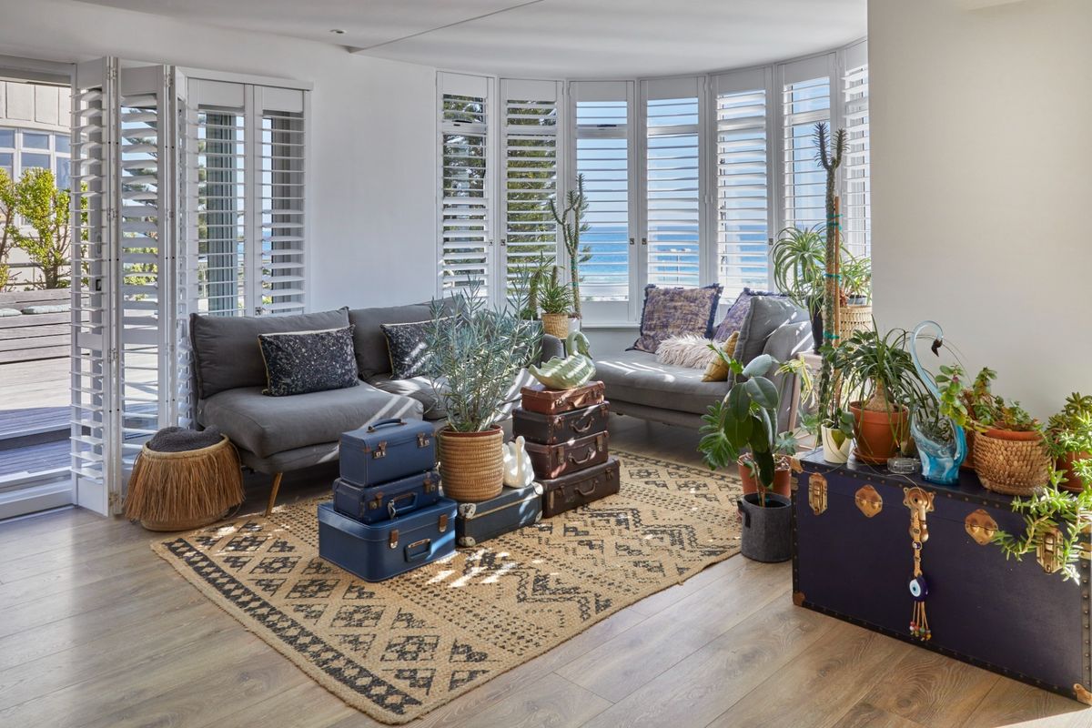 Bright living room featuring timber flooring, plantation shutters, and bi-fold doors opening to an outdoor deck with ocean views.