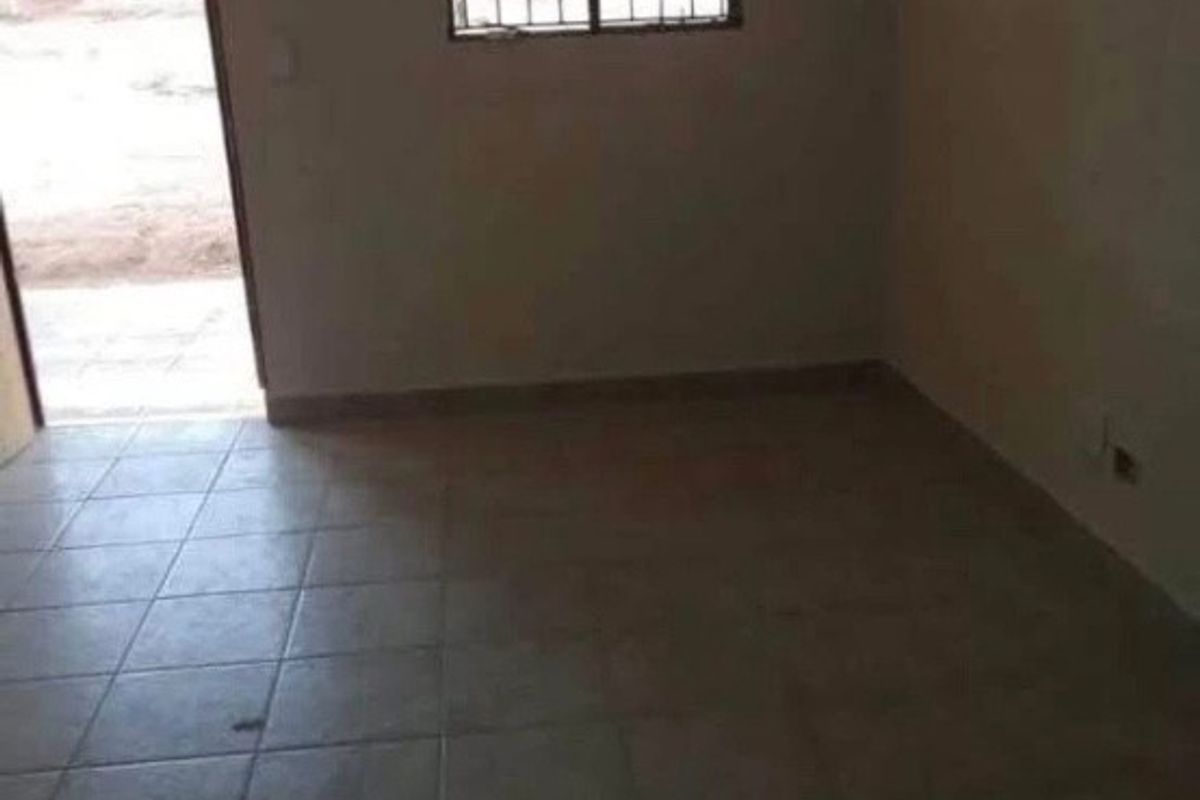 An empty, neutrally painted living area featuring tiled flooring and a sliding door leading to the exterior.
